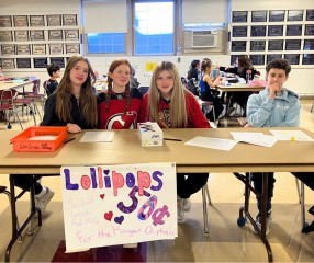 smiling middle school students sitting at a table selling lollipops